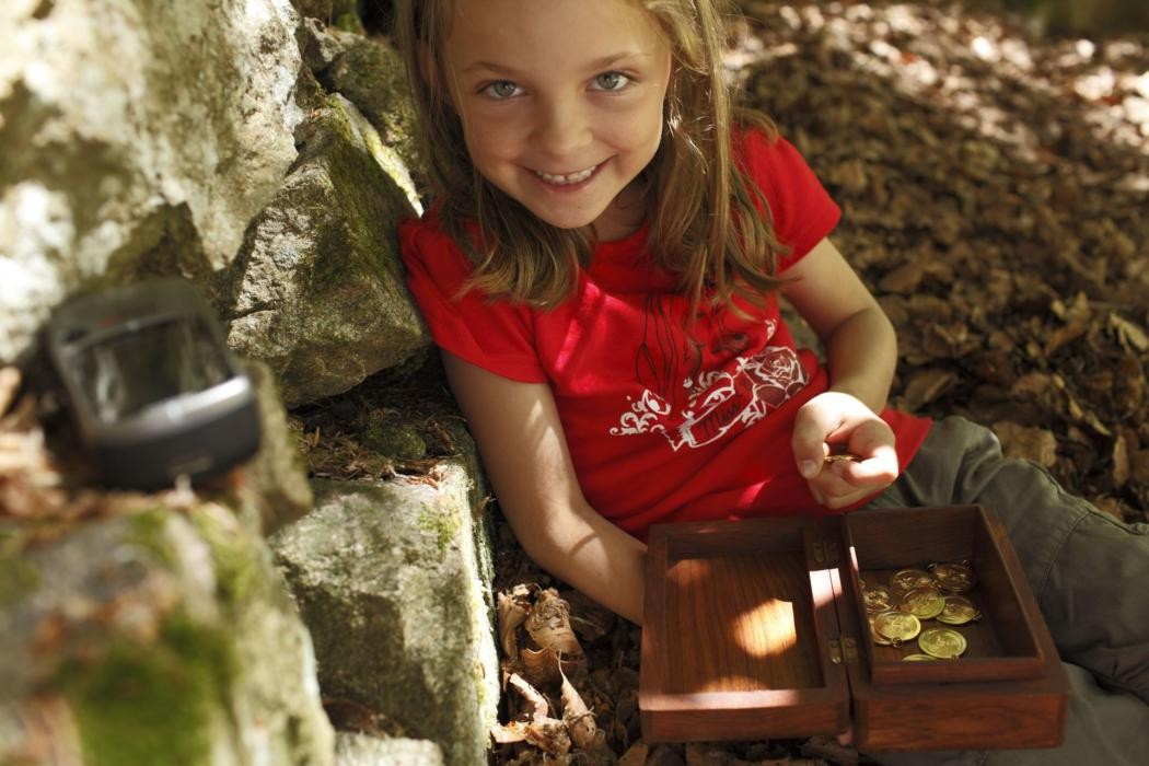 Ein lachendes Mädchen mit einer Truhe voll Gold in der Hand sitzt auf dem Waldboden